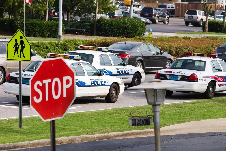 cars and police cars all parked together in front of a stop sign