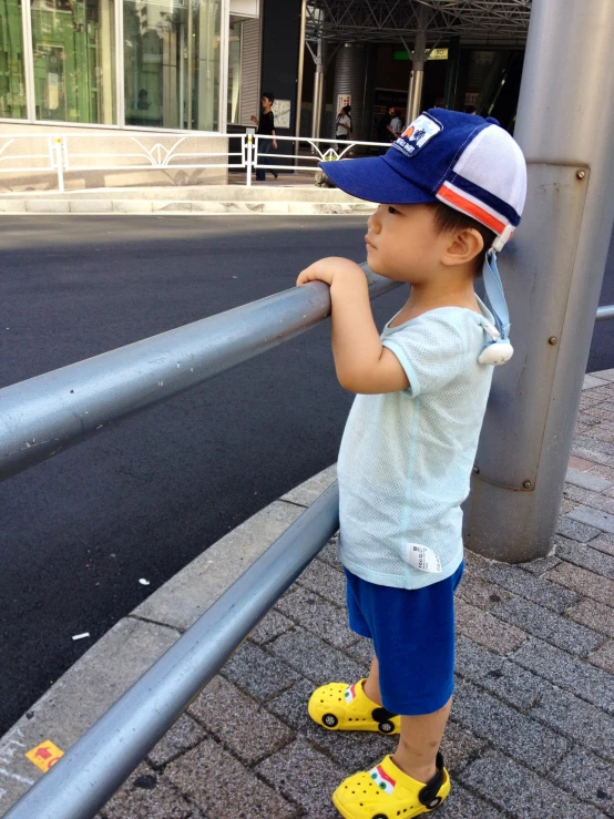 a small boy is wearing a blue hat standing next to a fence