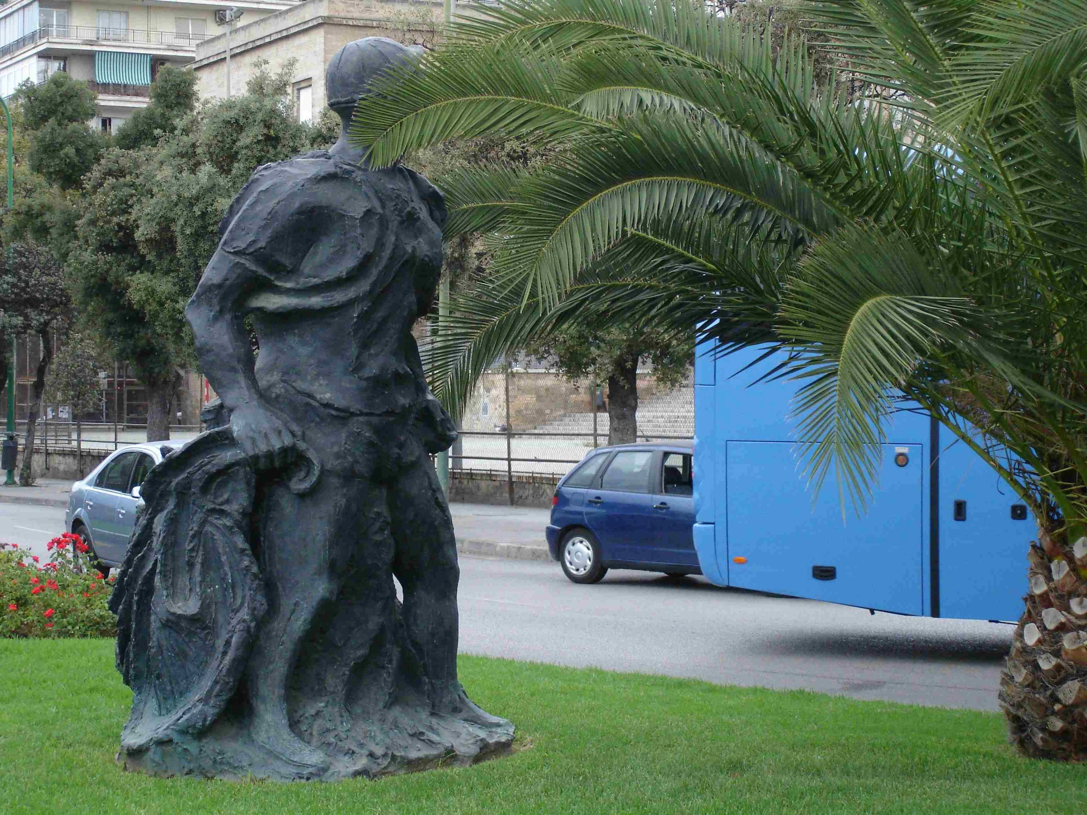 the sculpture is sitting in front of a blue bus