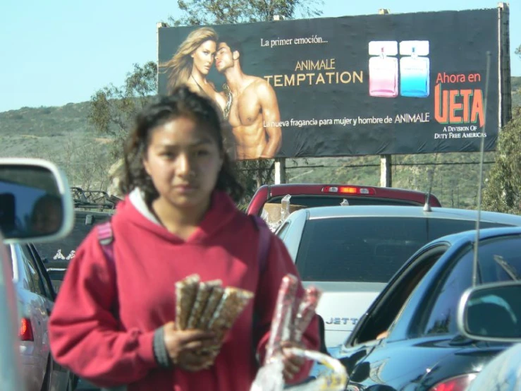 a woman in a red hoodie stands by a parking lot holding a bag