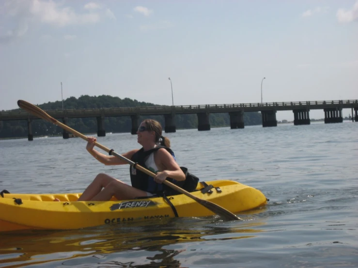 a woman in a kayak paddles near a bridge