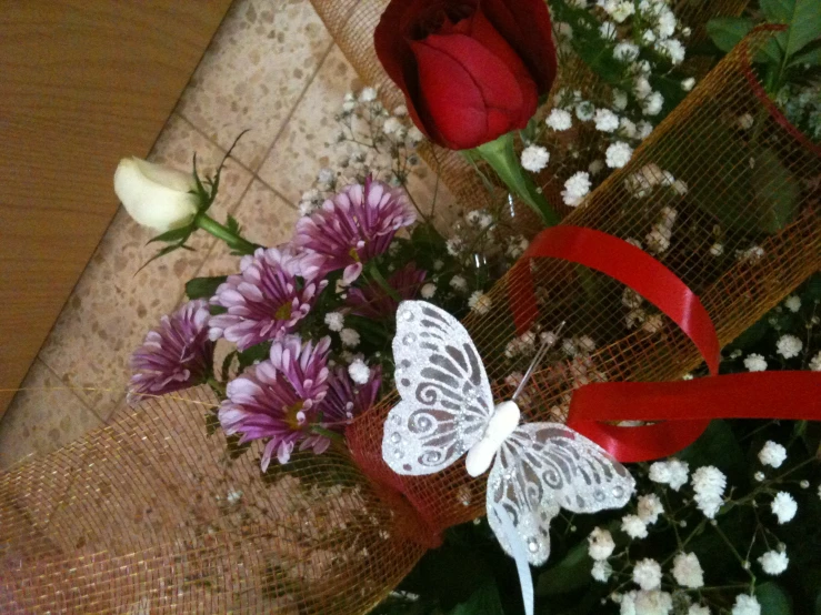 a white erfly is perched on the red ribbon and flowers