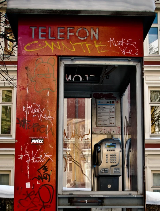 an old telephone on the street with graffiti all over