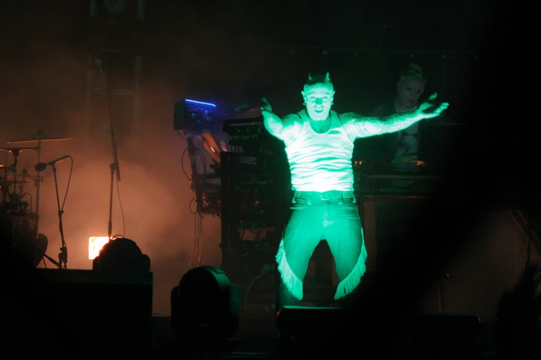 man in green pants with arms out at concert