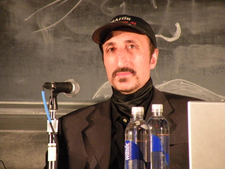 a man wearing a hat sits behind a microphone