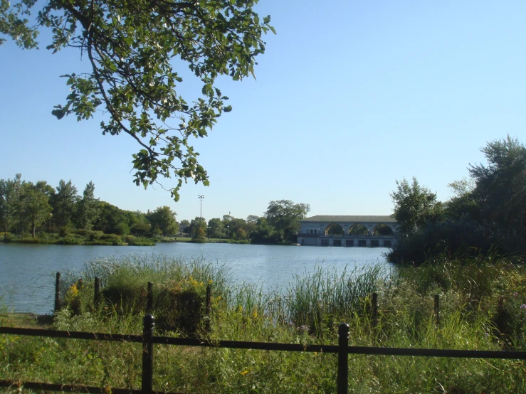 a body of water with trees, fence and houses