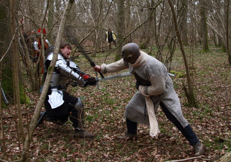 two men in medieval costumes are fighting in the woods