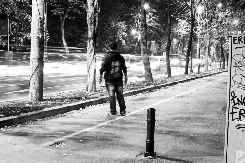 a young man with a backpack walking by some graffiti covered trees