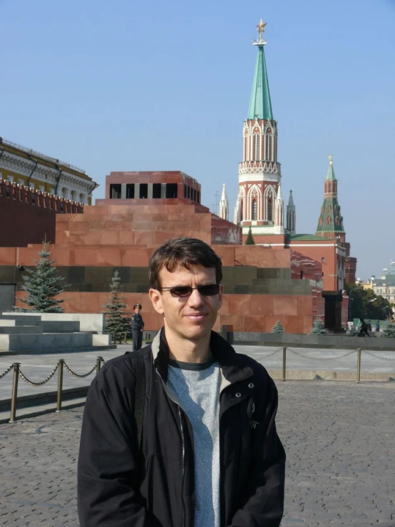 man wearing sunglasses standing near a church with large buildings