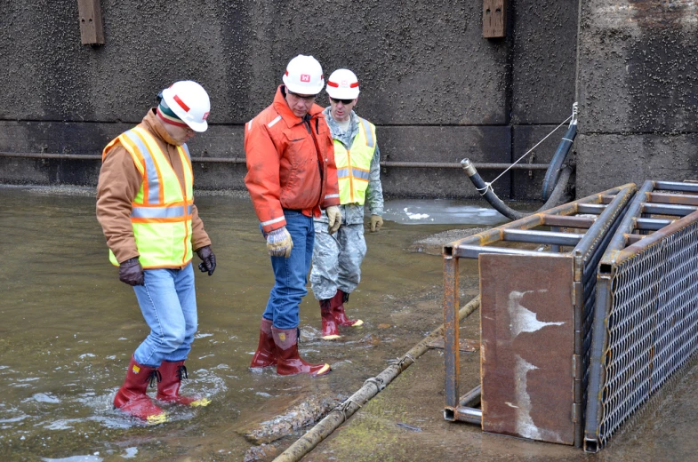 men in orange vests and red helmets standing by some trash bins