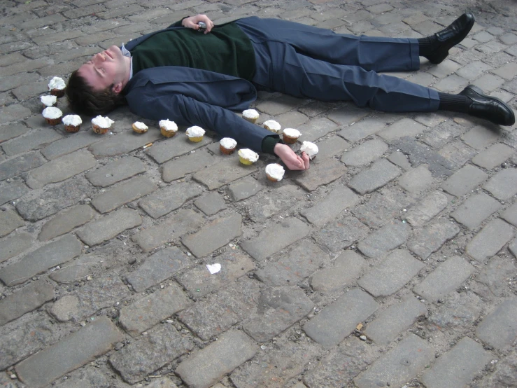 a man wearing a suit and tie laying on the ground with cupcakes around him