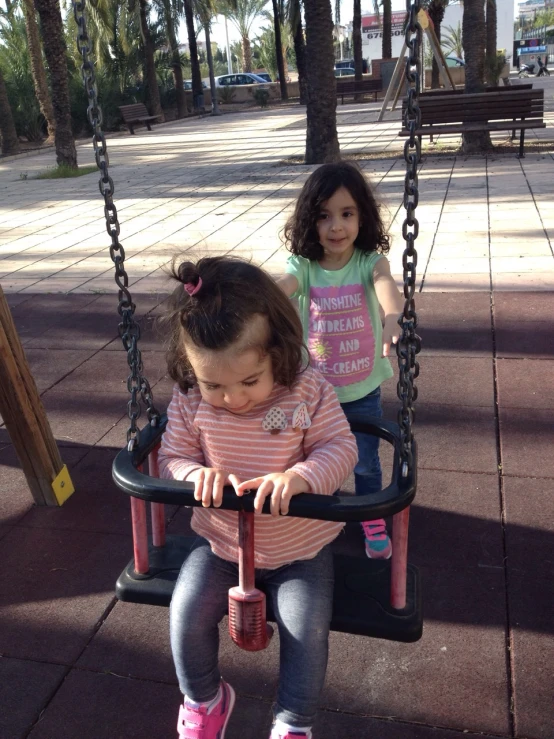 two little girls are sitting in a swing together