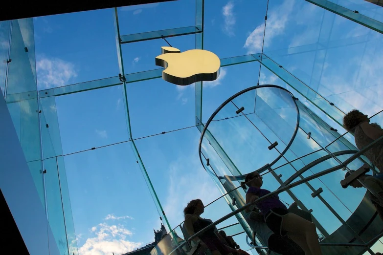 several people standing inside of glass with a apple logo hanging overhead