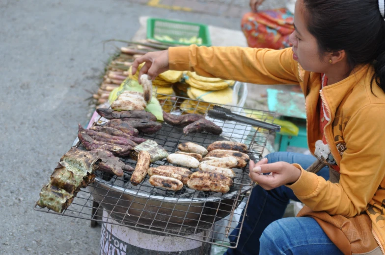 a woman sitting at an outdoor grill cooking food