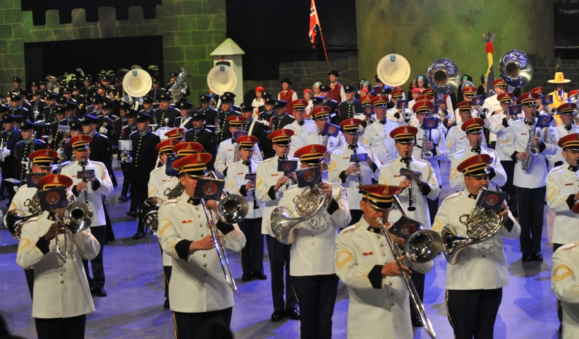 the band in white uniforms are performing with silver trombones