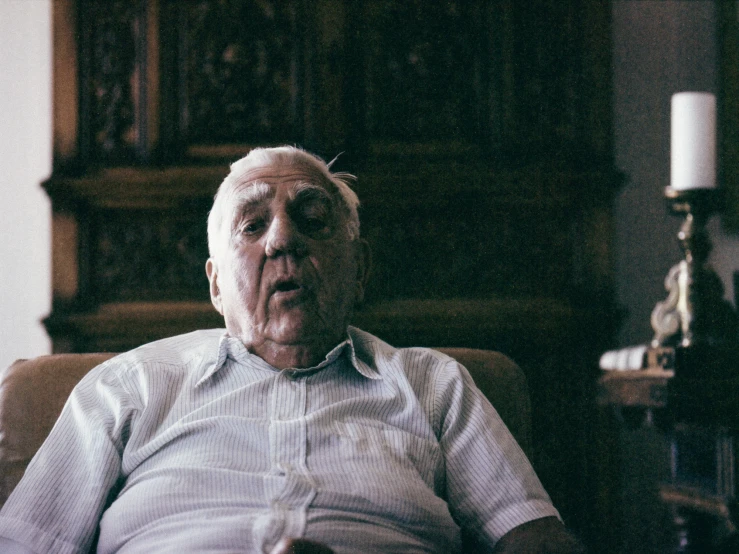 an older man wearing glasses sitting in a chair with a book in his hand