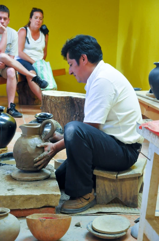 a man sitting down with pottery on a table