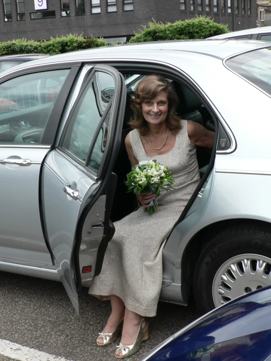 a woman is exiting a car wearing a dress and holding flowers