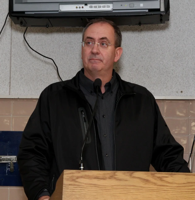 a man standing behind a wooden table giving a speech