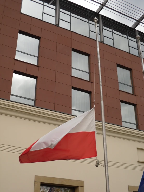 a very tall red and white flag flying next to a brown building