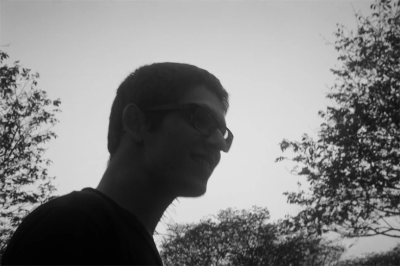 a man wearing glasses standing in front of trees