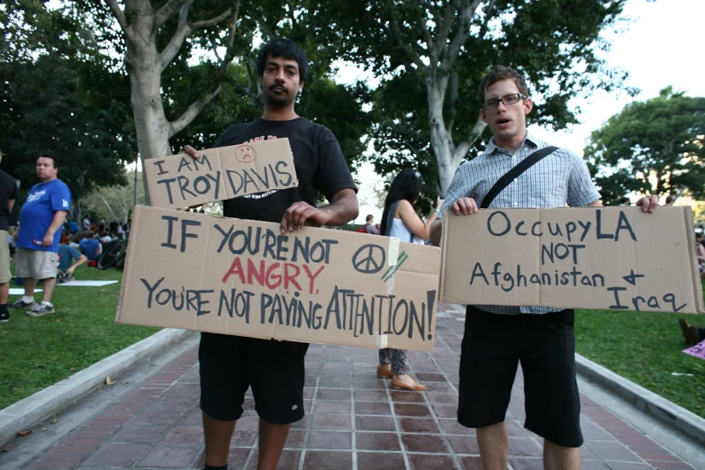two young men holding signs that read if you're not angry you're not paying attention