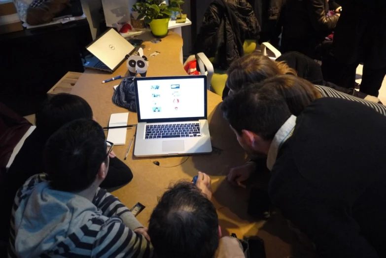 four men and one woman are at a desk with a laptop