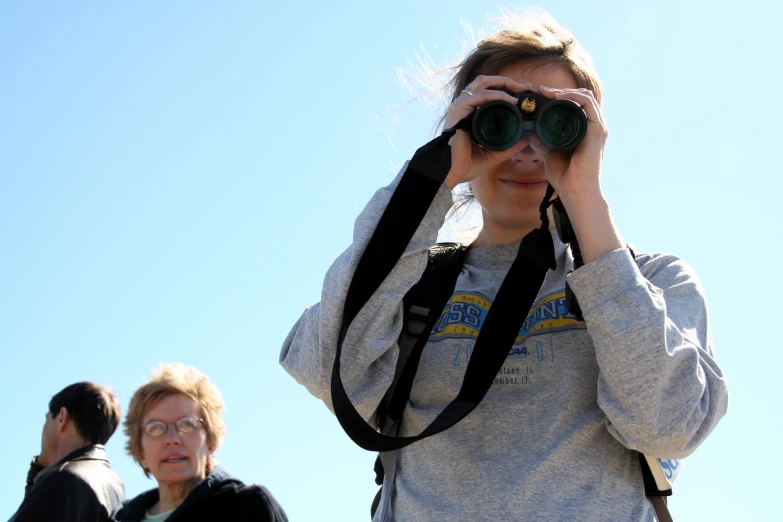 a girl looks into a pair of binoculars while people look on