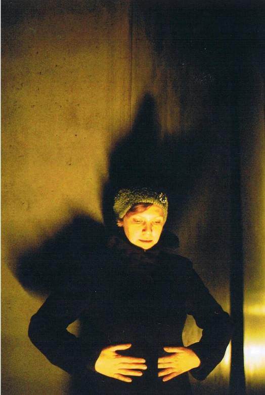 a woman poses in the shadows, against the wall