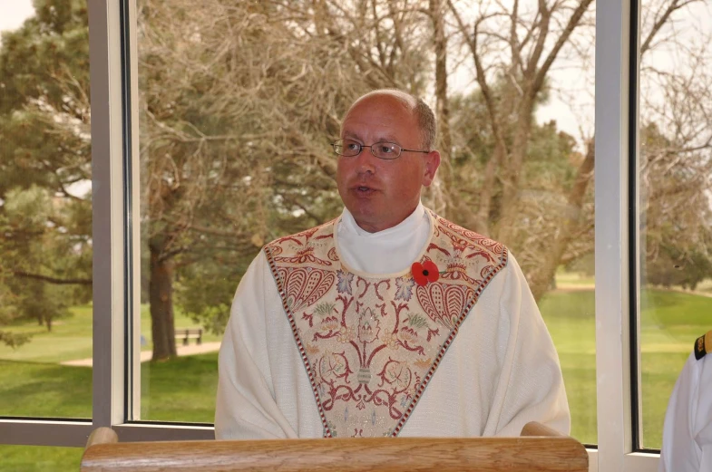 priest wearing white clothes sitting in front of stained glass windows