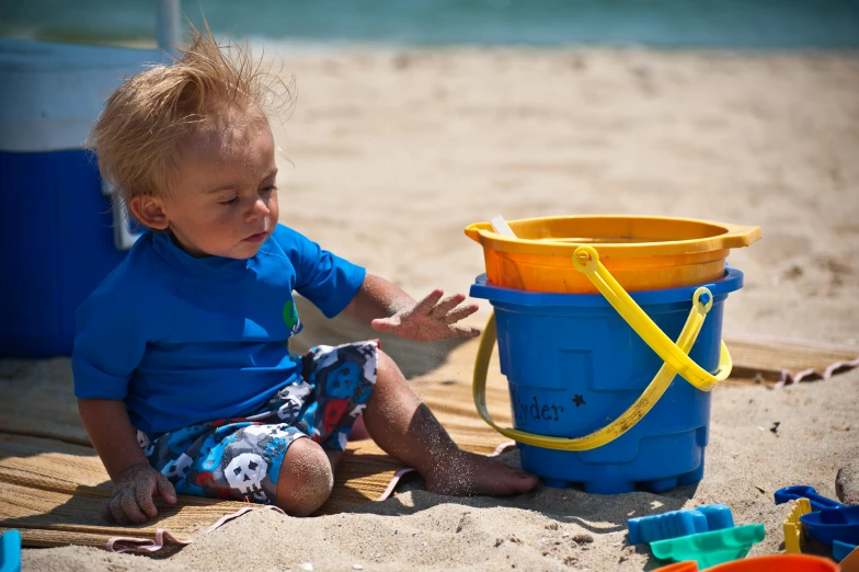 the baby boy sitting near a blue bucket