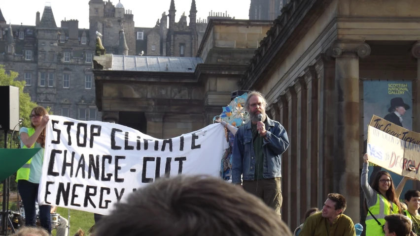 an older man holding a protest sign while talking on a microphone