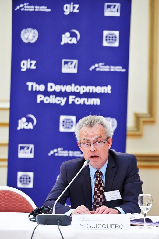 man talking on microphone in front of conference banner