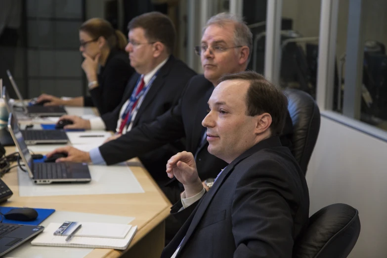 a group of men sitting at a table using laptop computers