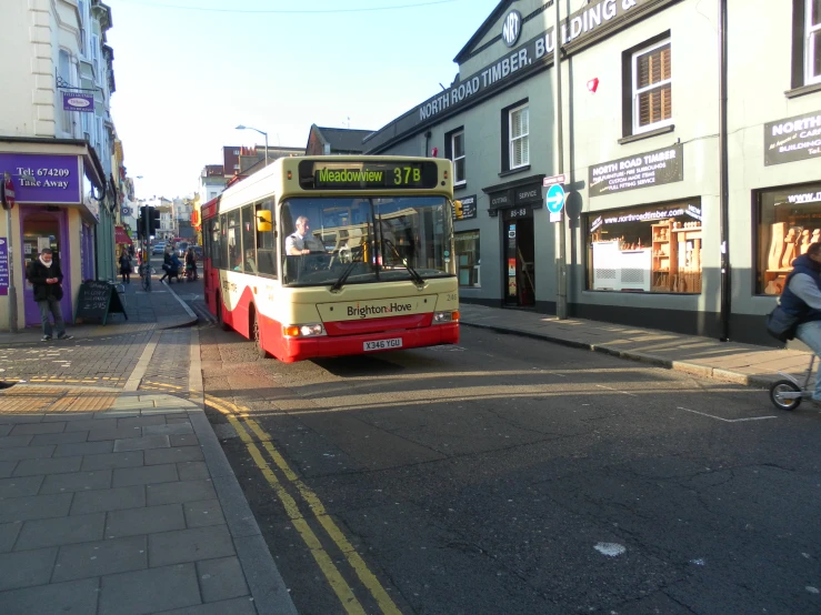 a city bus driving on the road past some shops
