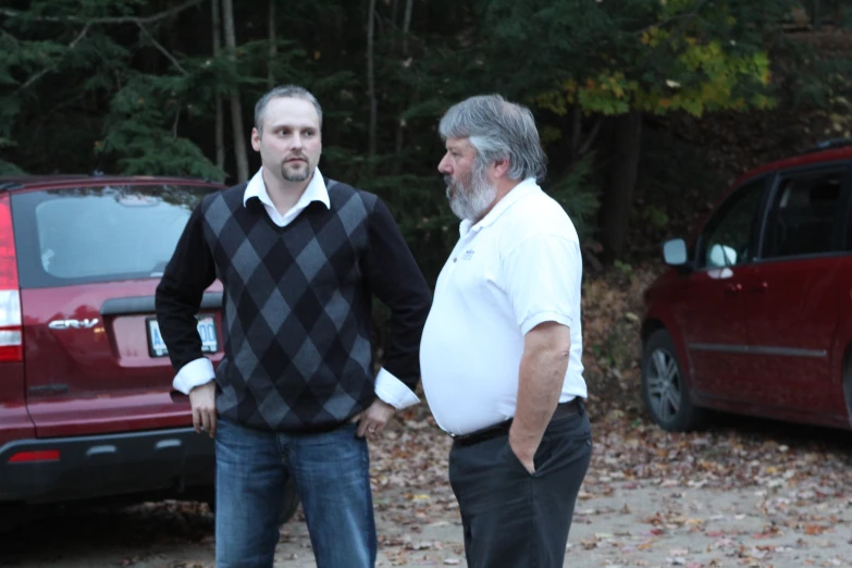 two men are facing each other in front of two parked cars