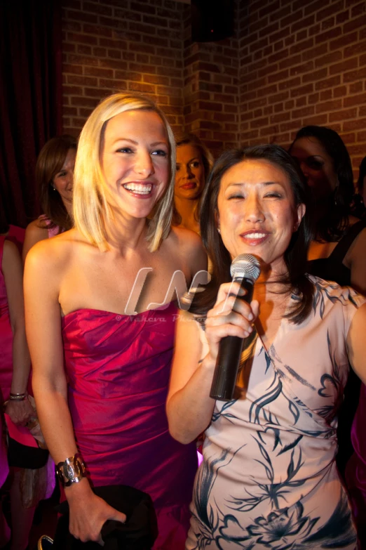 two young women in pink dresses singing into microphone