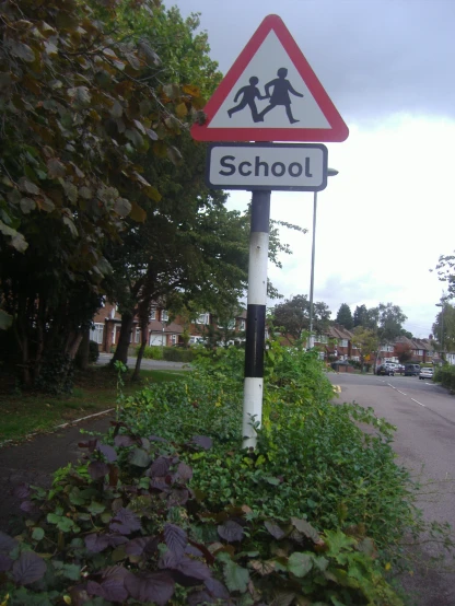 the children are crossing on the sidewalk in front of the school sign