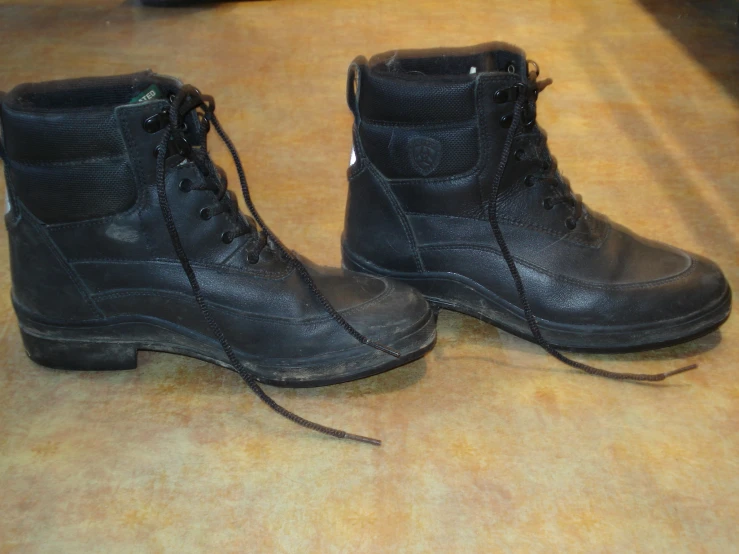 a pair of black leather boots sitting on top of a wooden floor