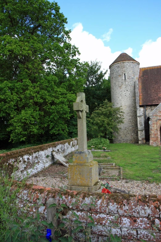 old looking cross in a graveyard with brick buildings and green trees