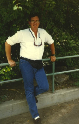 a man poses for the camera while leaning on a fence