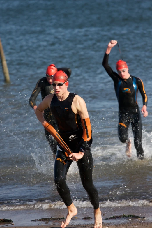 three people are wetsuits running through the water