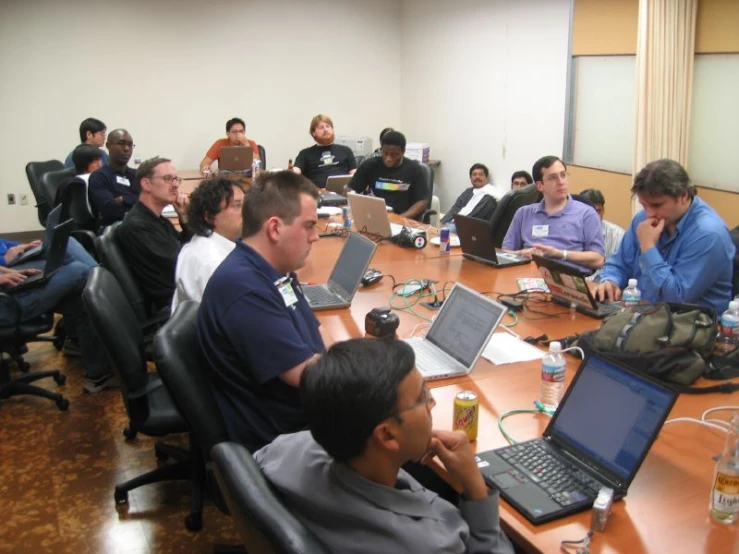 a group of people sitting around a table with laptop computers on top of them