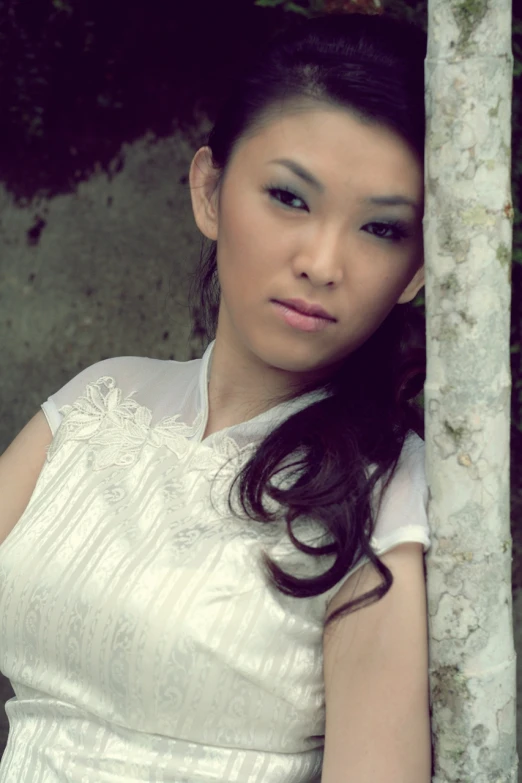 a young woman posing against a tree trunk