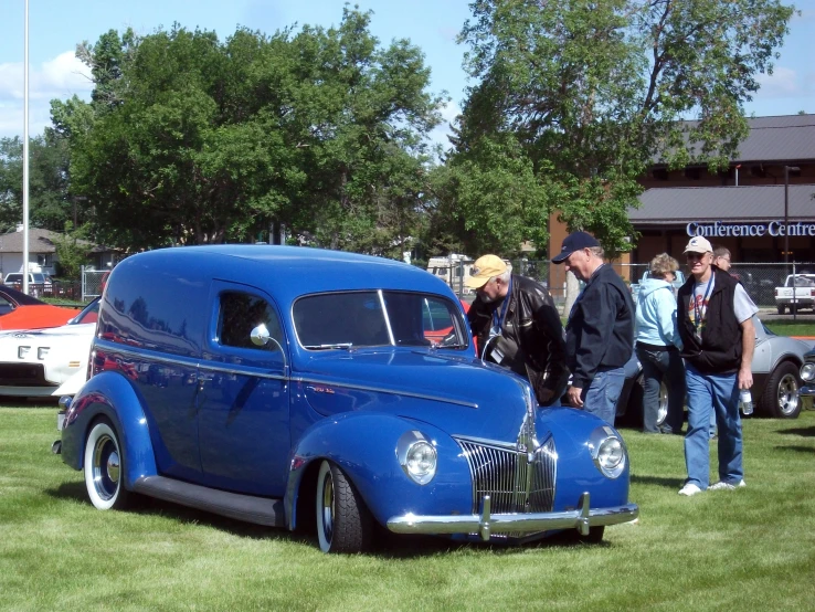 several people gathered around a classic blue car on a field