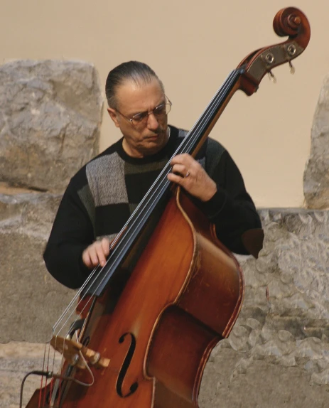 a person holding a bass, while standing next to a stone wall