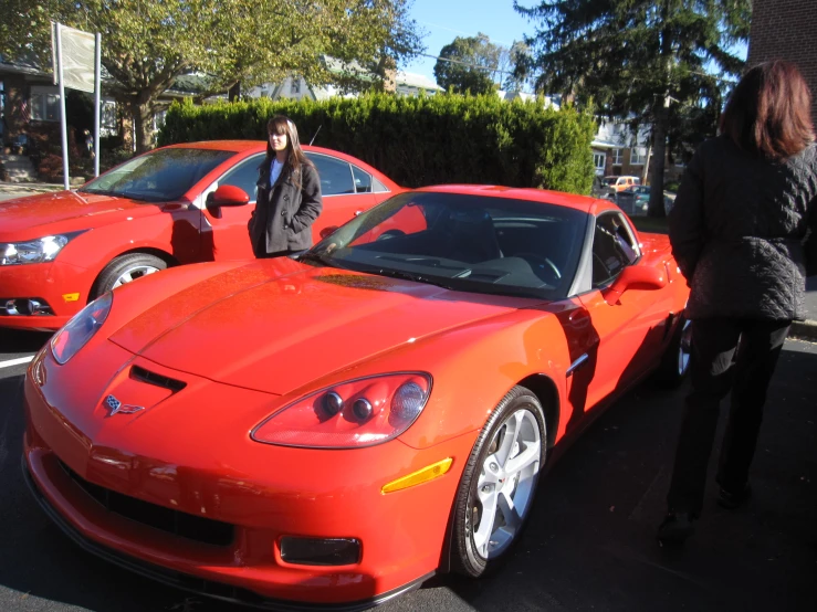 two women stand next to the red sports cars parked beside each other