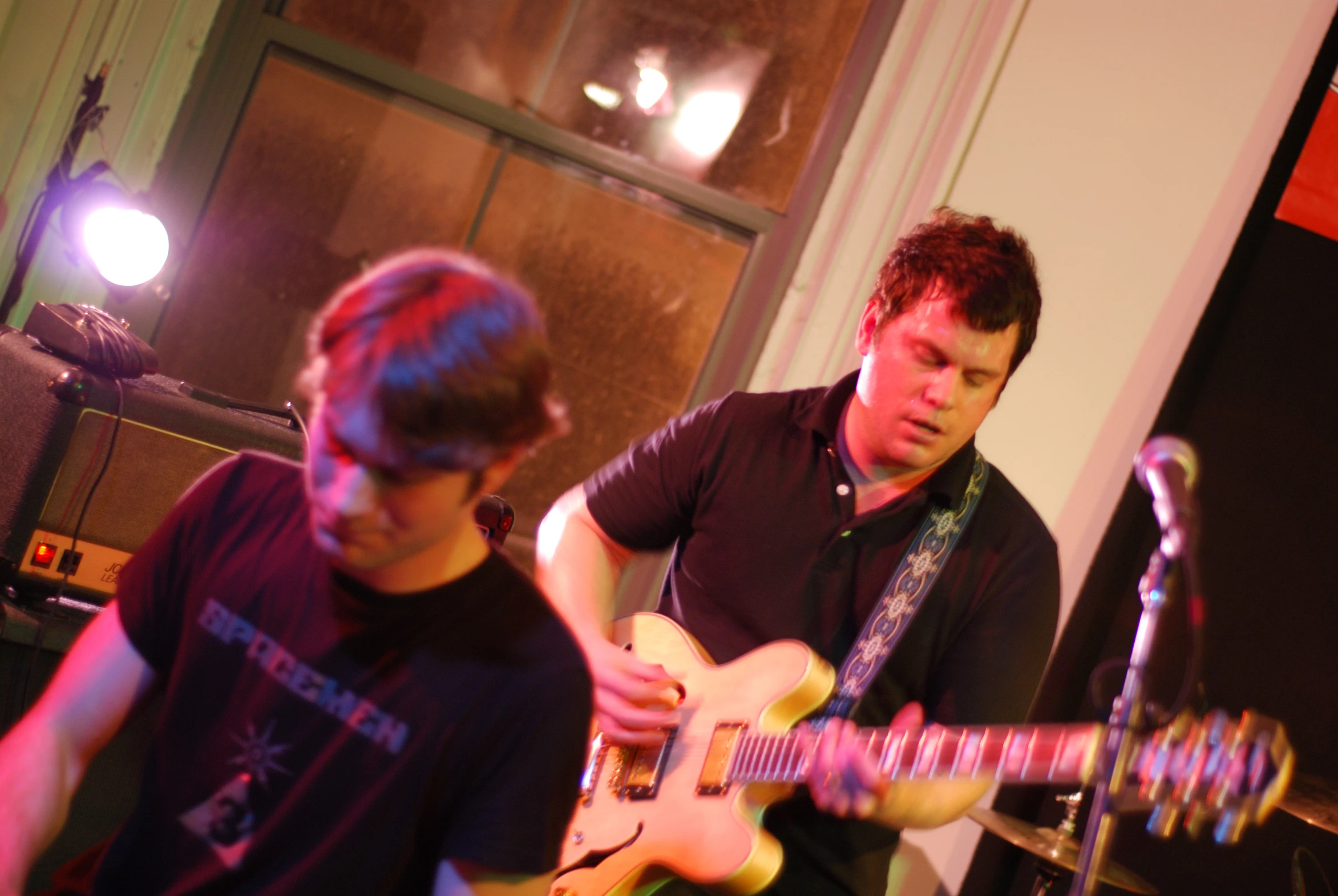 two men are playing guitar in front of microphones