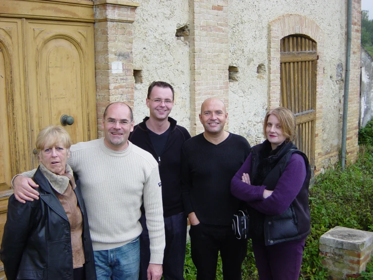 four people smiling at the camera in front of an old house