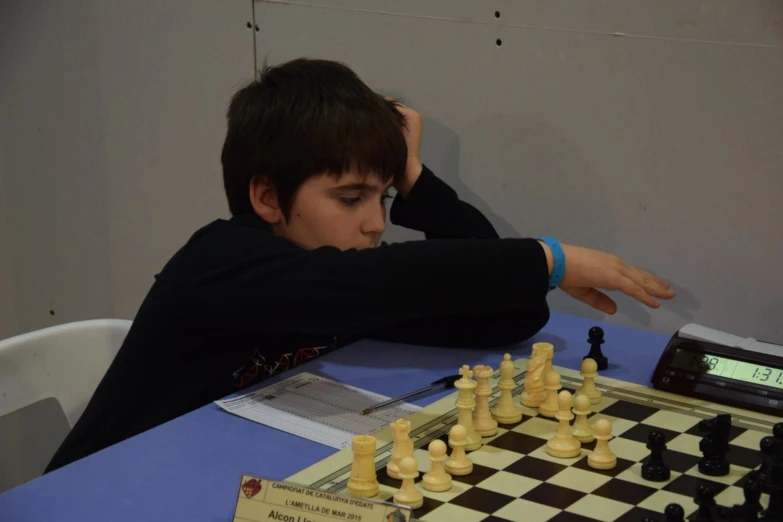 the boy plays chess in front of a digital clock